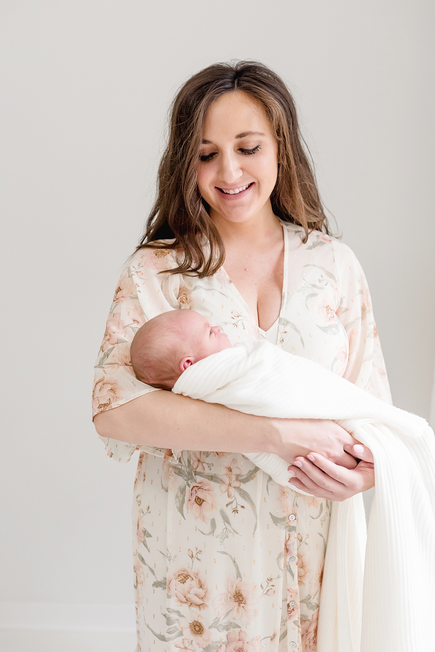New mom in floral print dress smiling down at newborn baby | Photo by Anna Wisjo Photography
