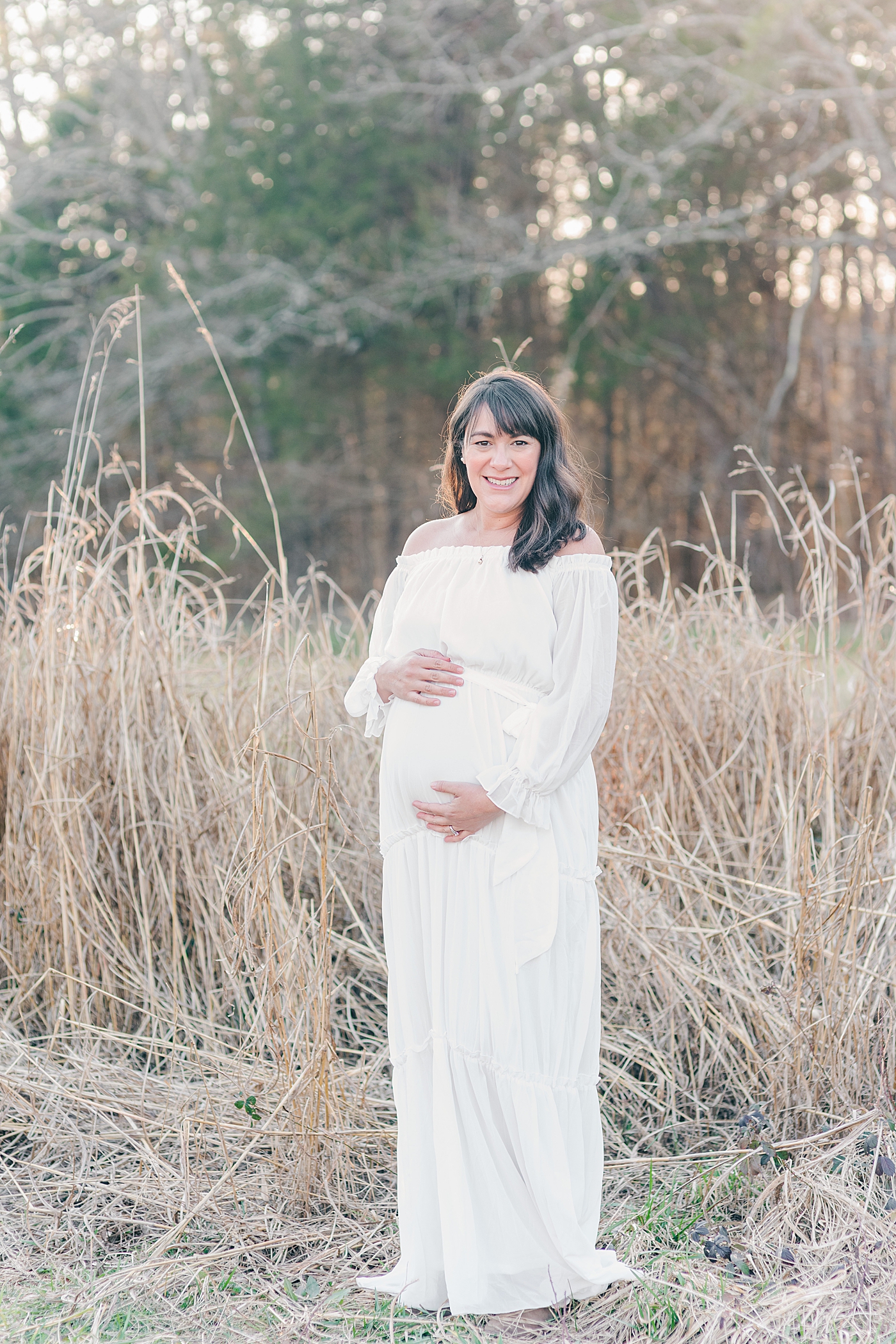 Smiling mom to be in a white dress | Photo by Anna Wisjo Photography