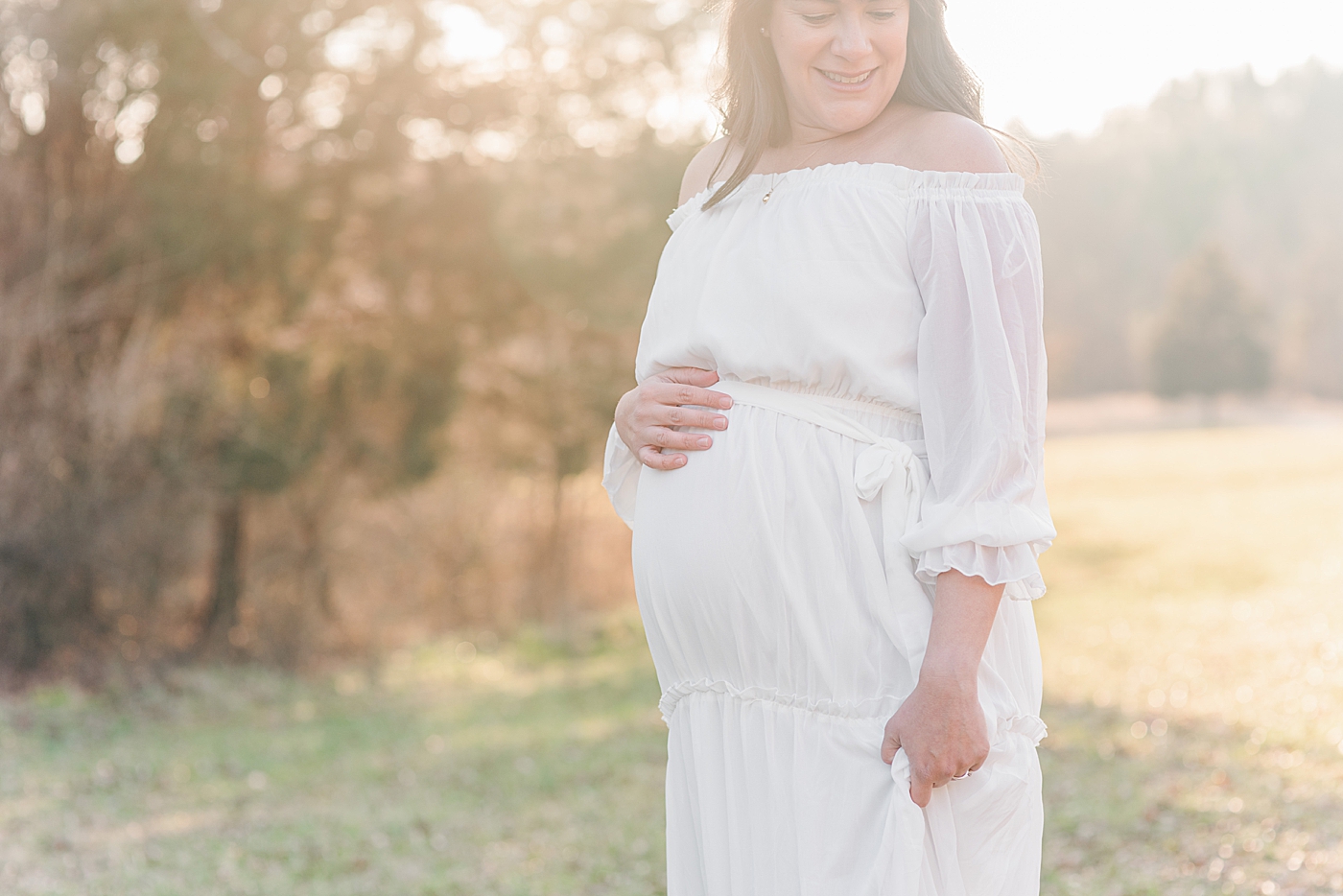 Pregnant woman in white dress in a field at sunset maternity session | Photo by Anna Wisjo Photography