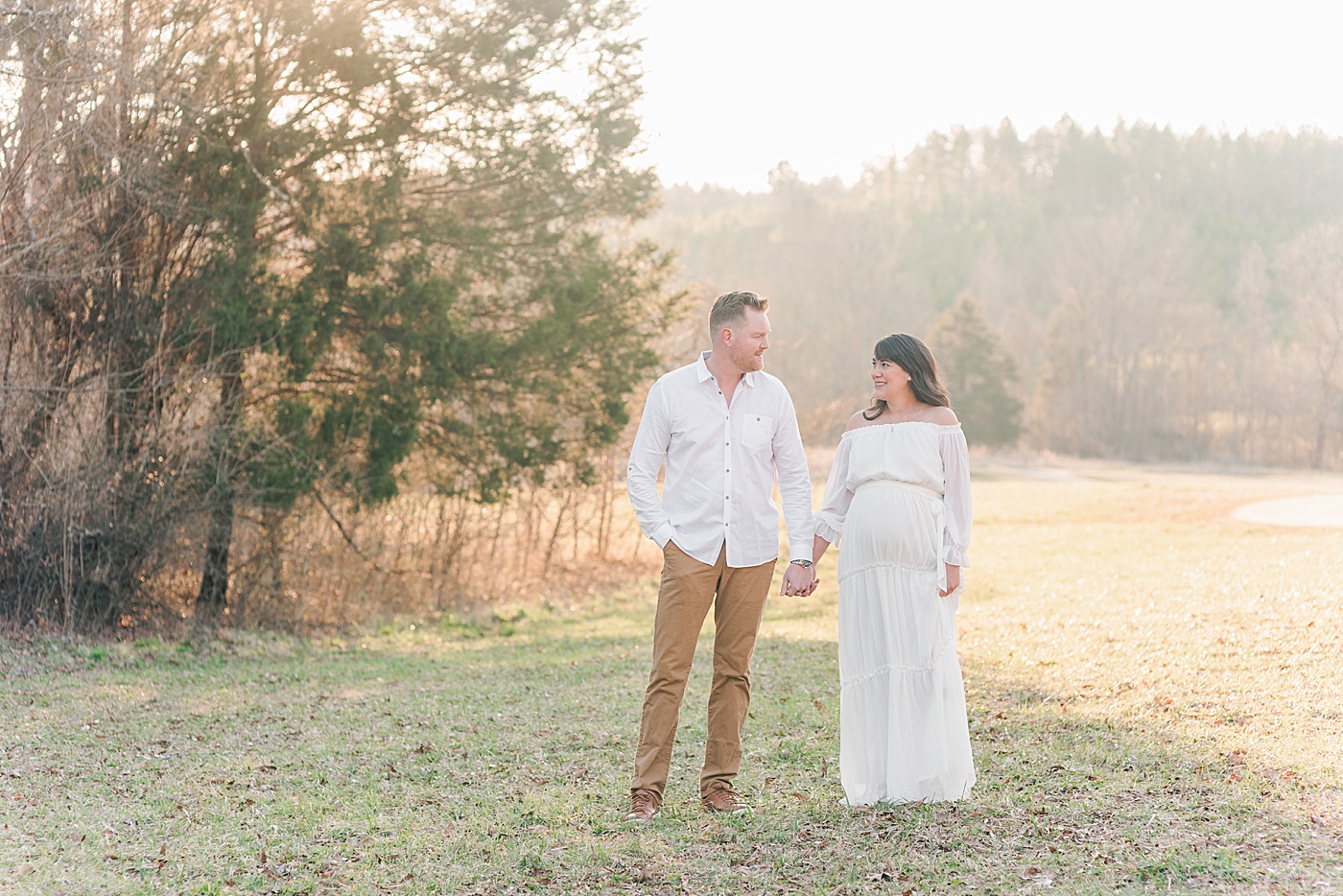 Mother and father to be holding hands in a field | Photo by Anna Wisjo Photography
