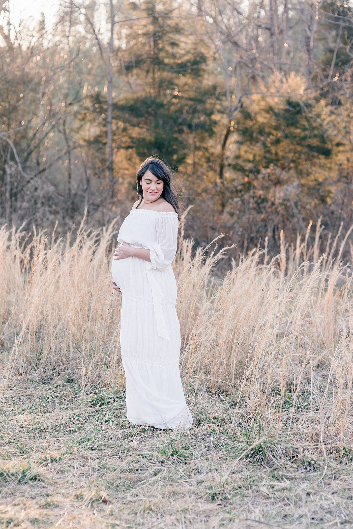 Mother to be in a white dress cradling her belly | Photo by Anna Wisjo Photography