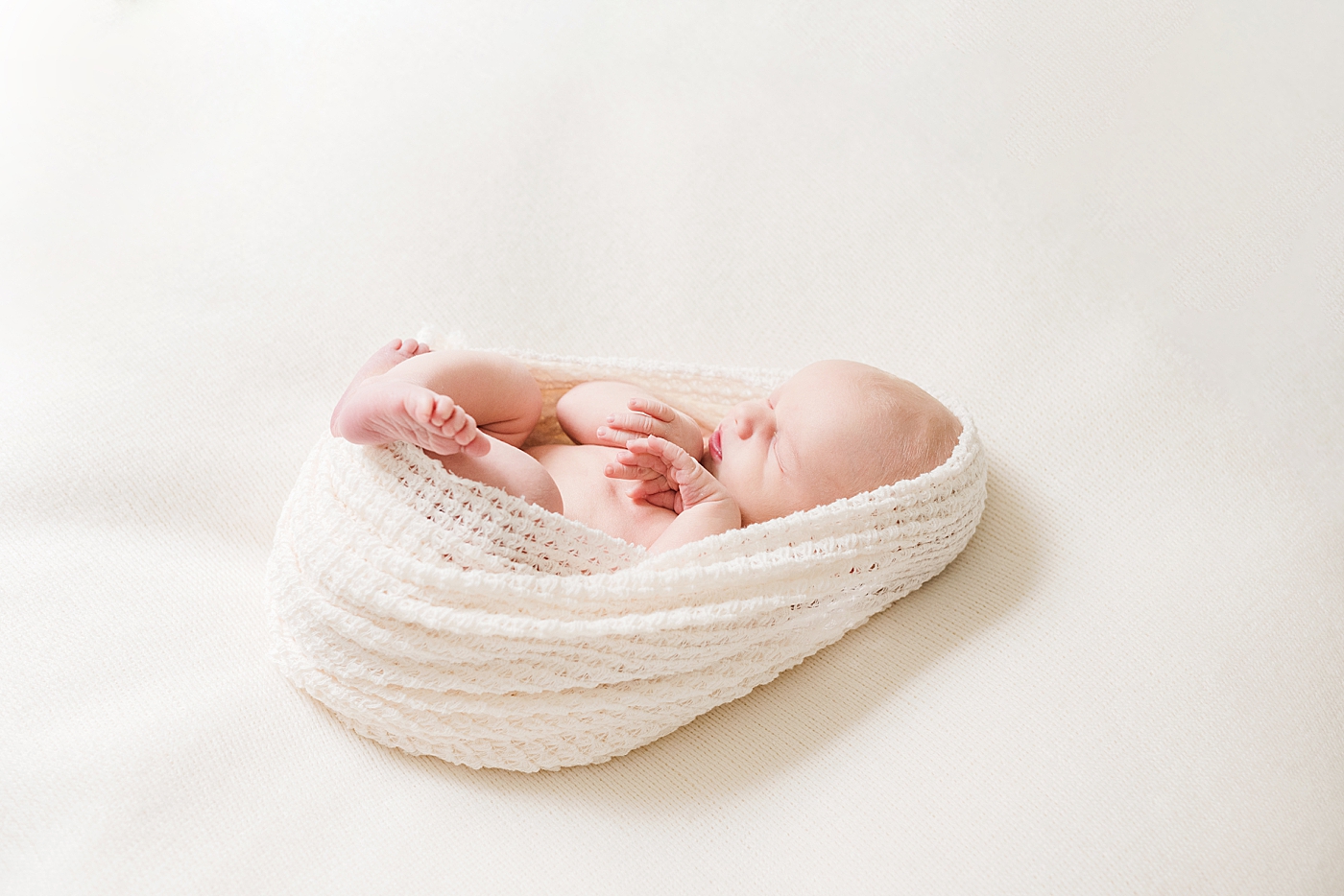 Side angle of newborn baby boy wrapped in cream swaddle | Photo by Anna Wisjo Photography