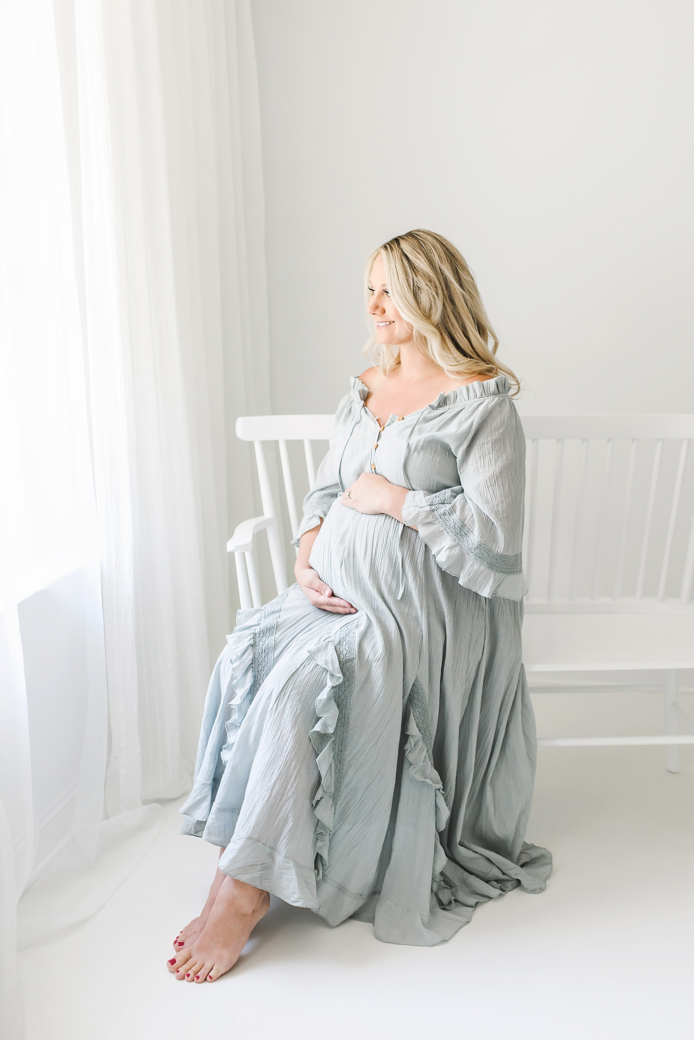 Pregnant woman in blue dress sitting on white bench | Photo by Huntersville Newborn Photographer Anna Wisjo 