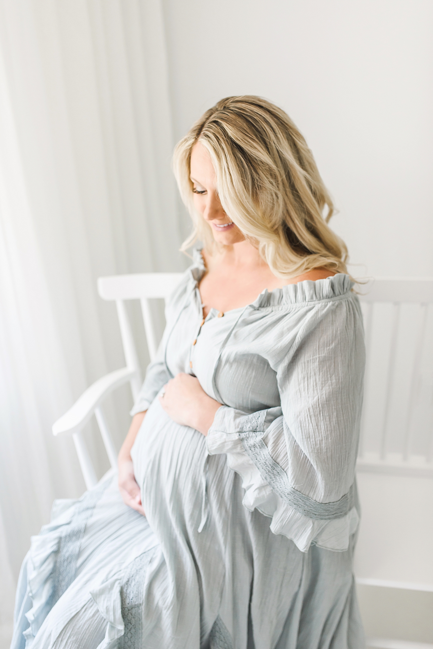 Pregnant woman in blue dress sitting on white bench | Photo by Anna Wisjo Photography
