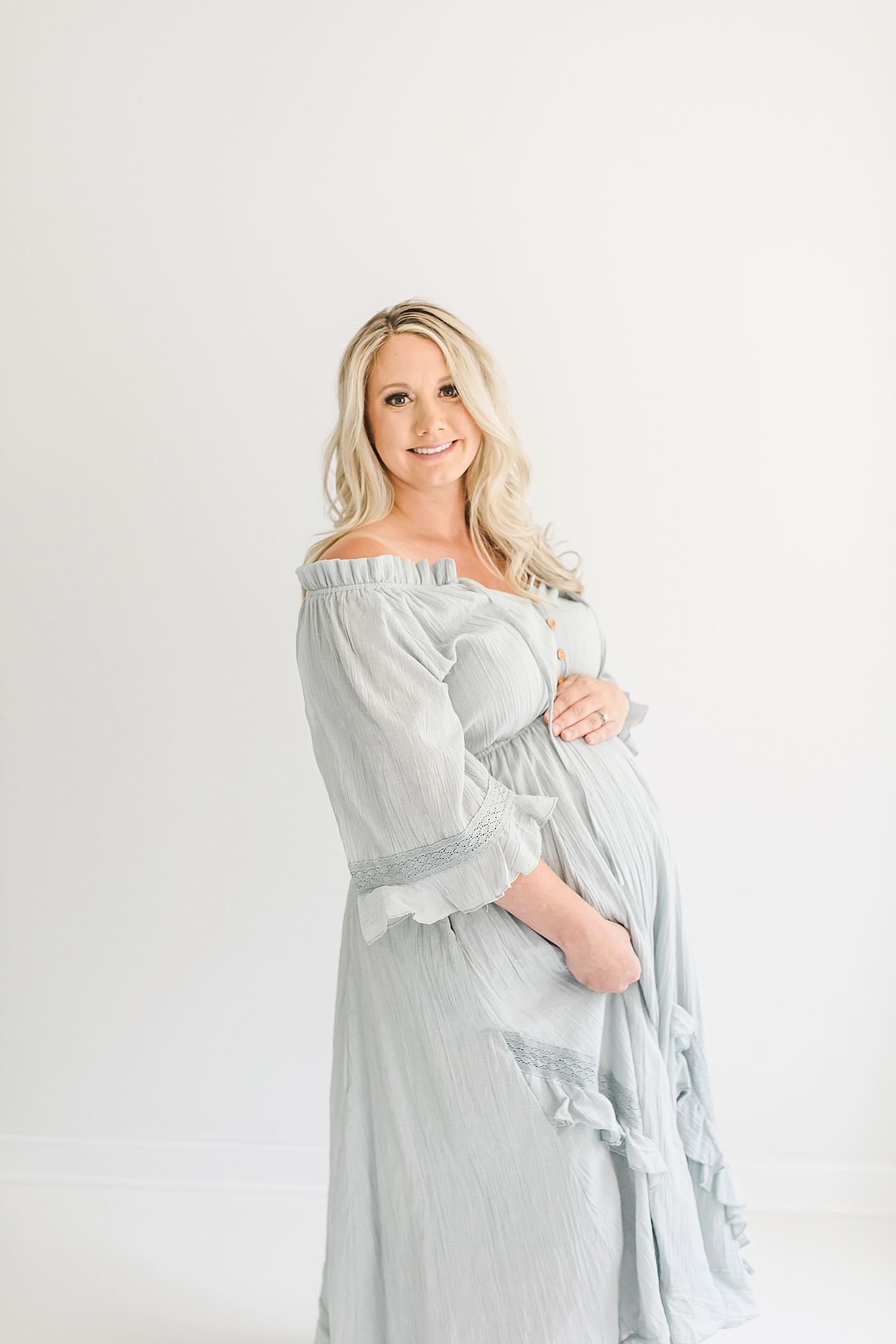 Mother to be in pale blue dress smiling at camera | Photo by Anna Wisjo Photography