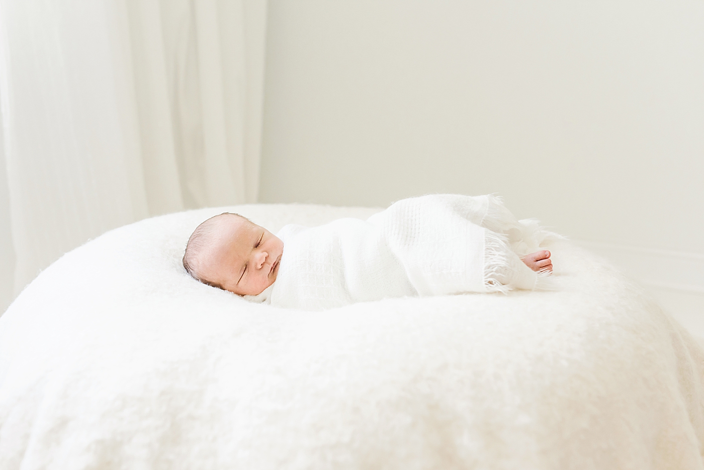 Sleeping newborn wrapped in white swaddle | Photo by Anna Wisjo Photography
