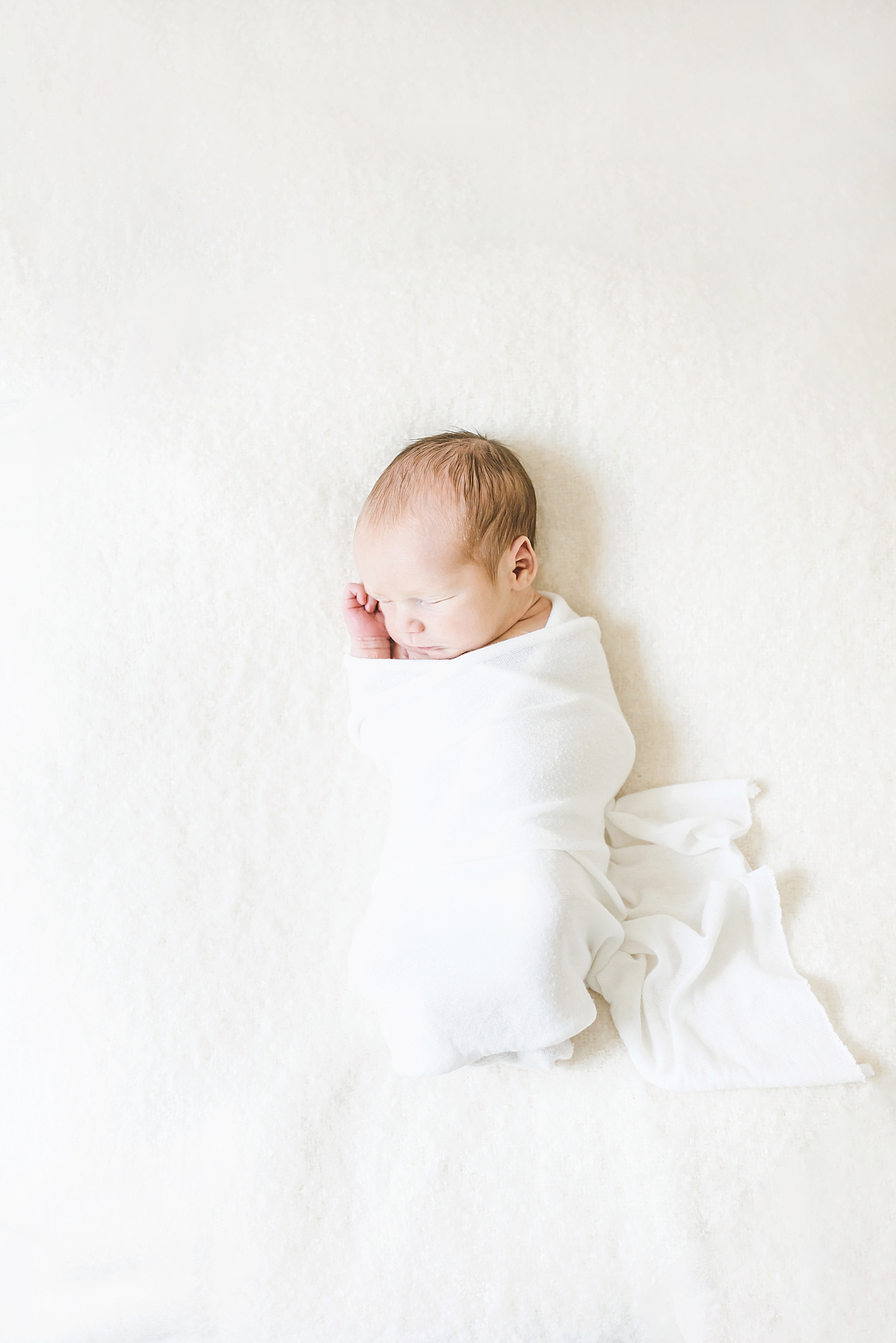 Newborn baby boy sleeping wrapped in white swaddle | Photo by Anna Wisjo Photography