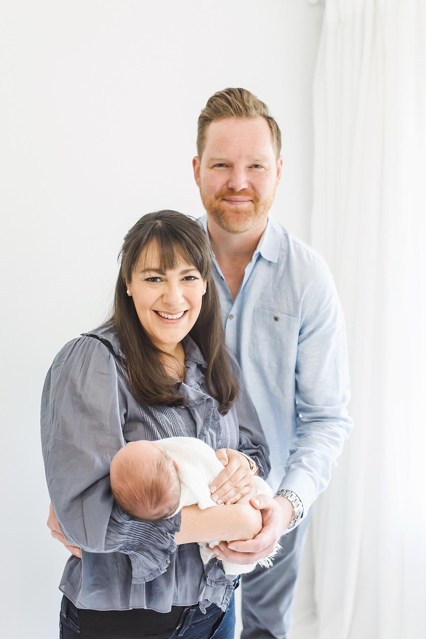 Mom and dad in blue with newborn baby boy smiling at the camera | Photo by Denver NC Newborn Photographer Anna Wisjo