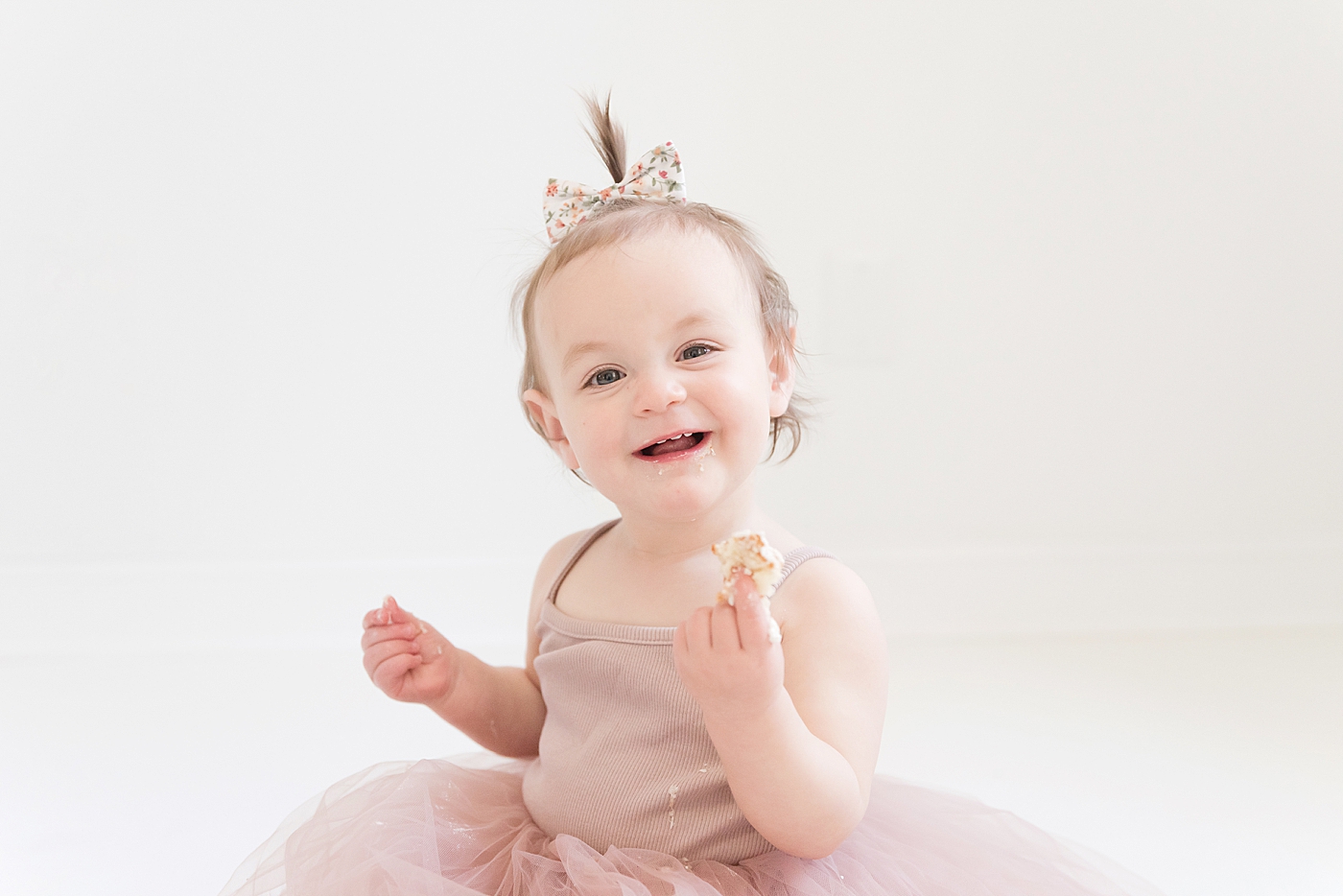 Toddler girl in pink smiling at the camera while eating cake| Photo by Anna Wisjo Photography