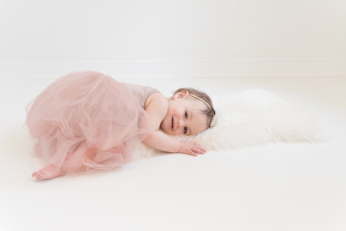 Baby girl in pink snuggling with soft white blanket looking at the camera | Photo by Anna Wisjo Photography