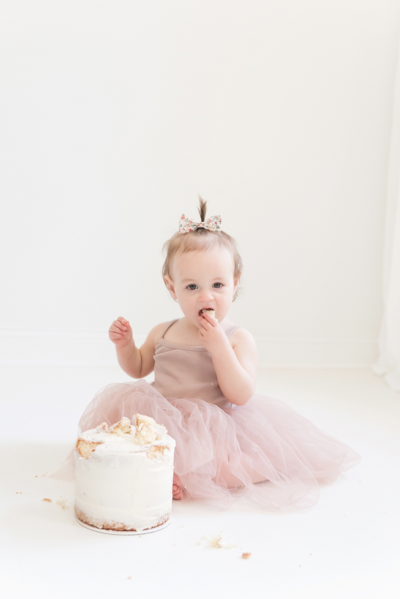 Baby girl in pink tutu with floral bow eating cake | Photo by Huntersville Baby Photographer Anna Wisjo 