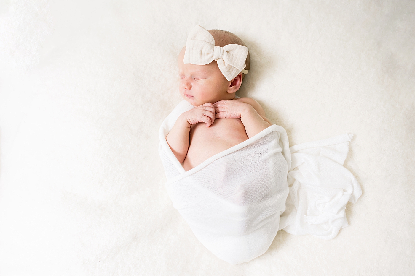 Newborn baby girl wrapped in white swaddle with bow | Photo by Huntersville NC Newborn Photographer Anna Wisjo