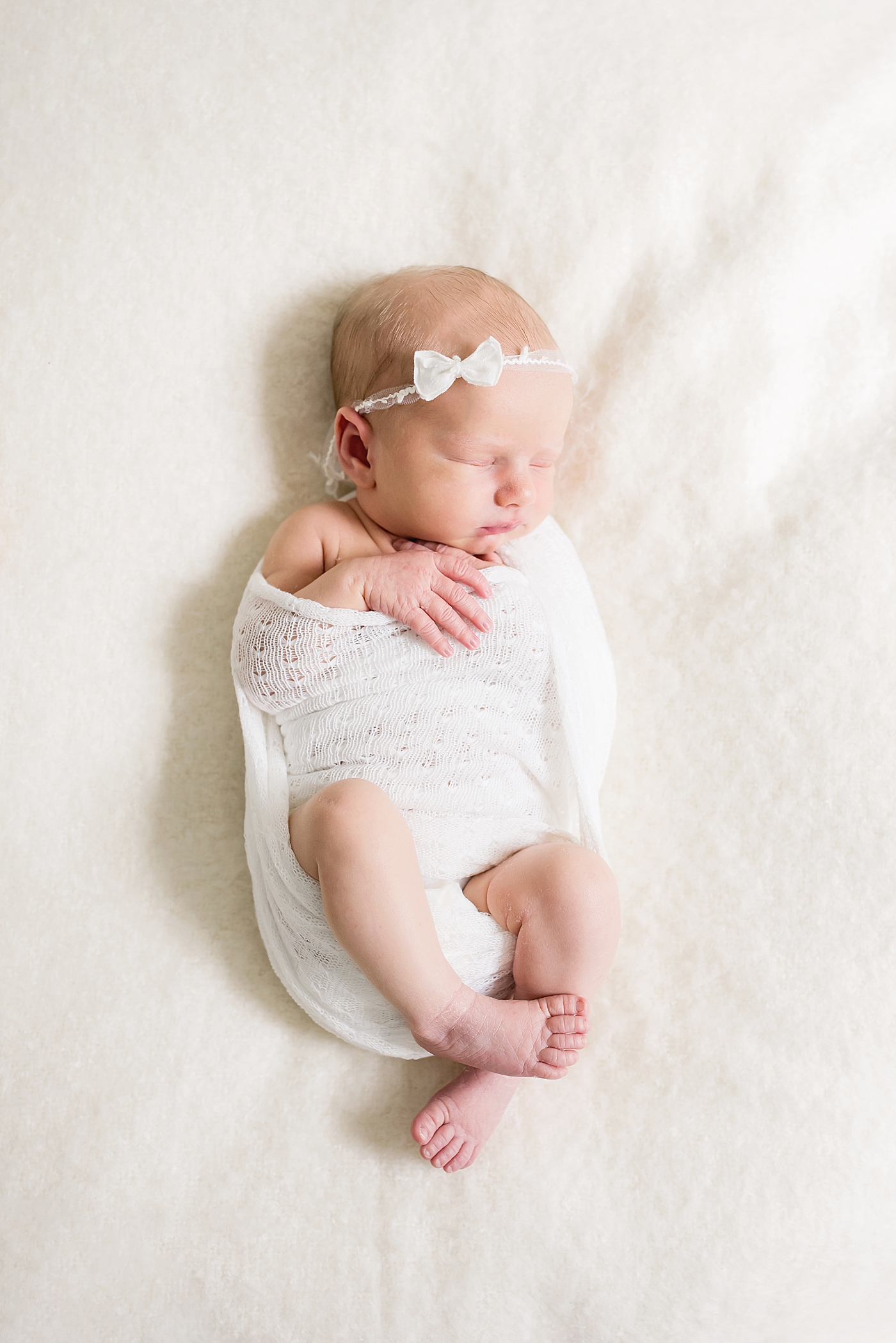 Baby girl with bow headband wrapped in white swaddle | Photo by Anna Wisjo Photography