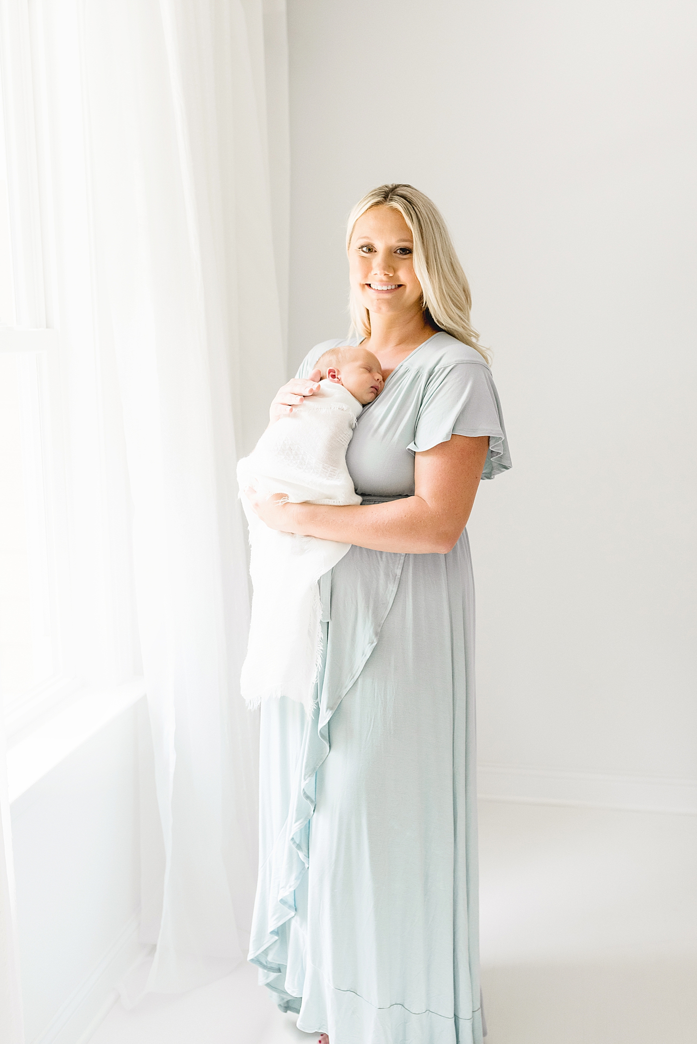Mom smiling at the camera while holding newborn baby girl | Photo by Anna Wisjo Photography