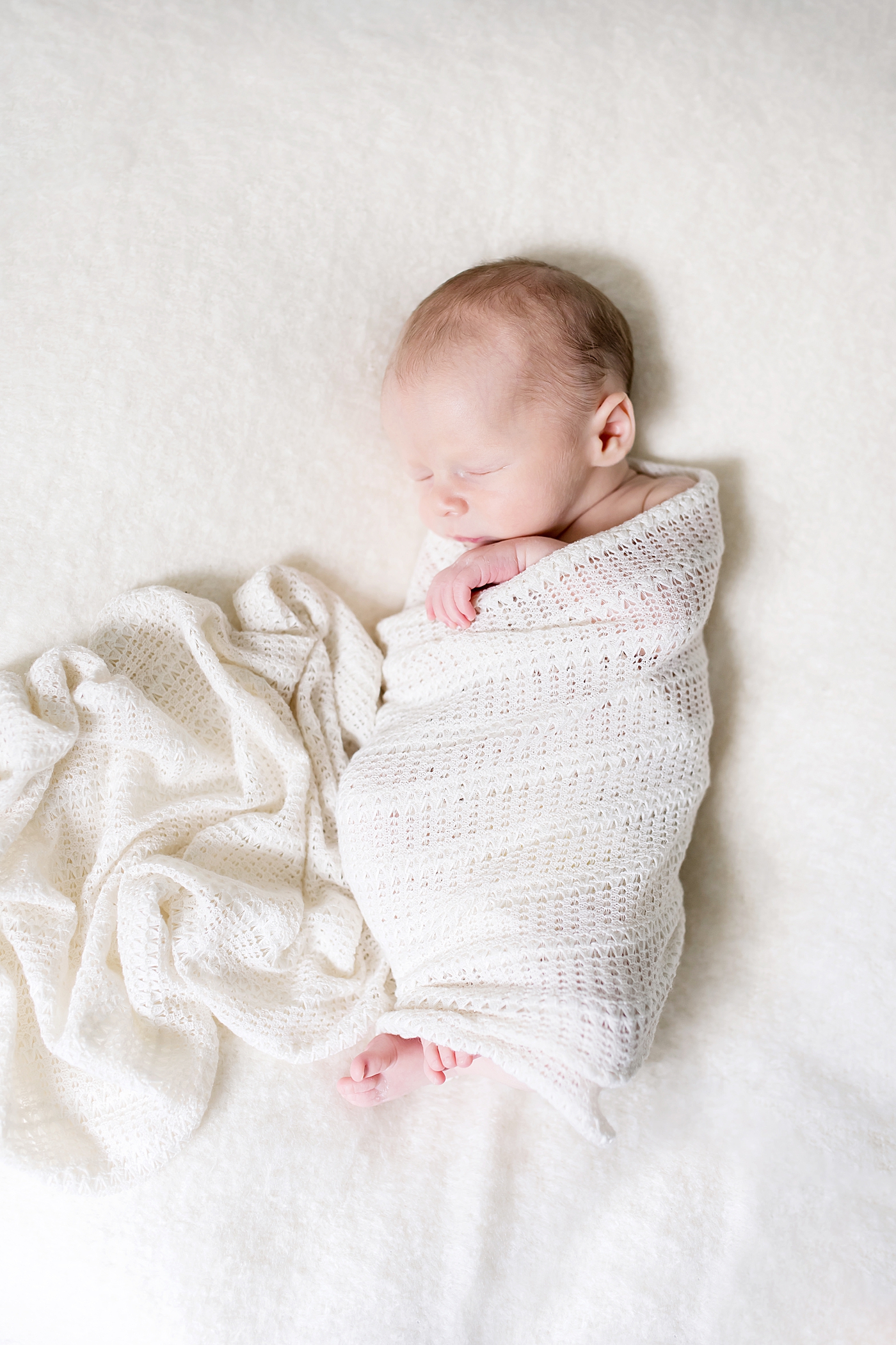 Baby boy wrapped in knitted white swaddle | Photo by Anna Wisjo