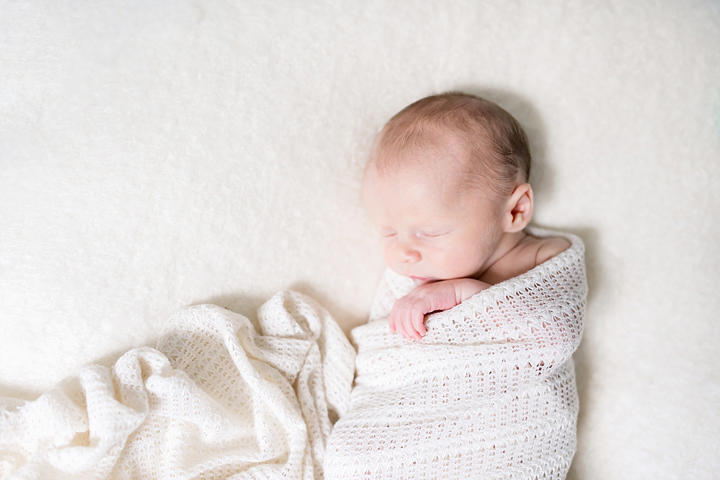 Newborn baby boy wrapped in white swaddle | Photo by Anna Wisjo