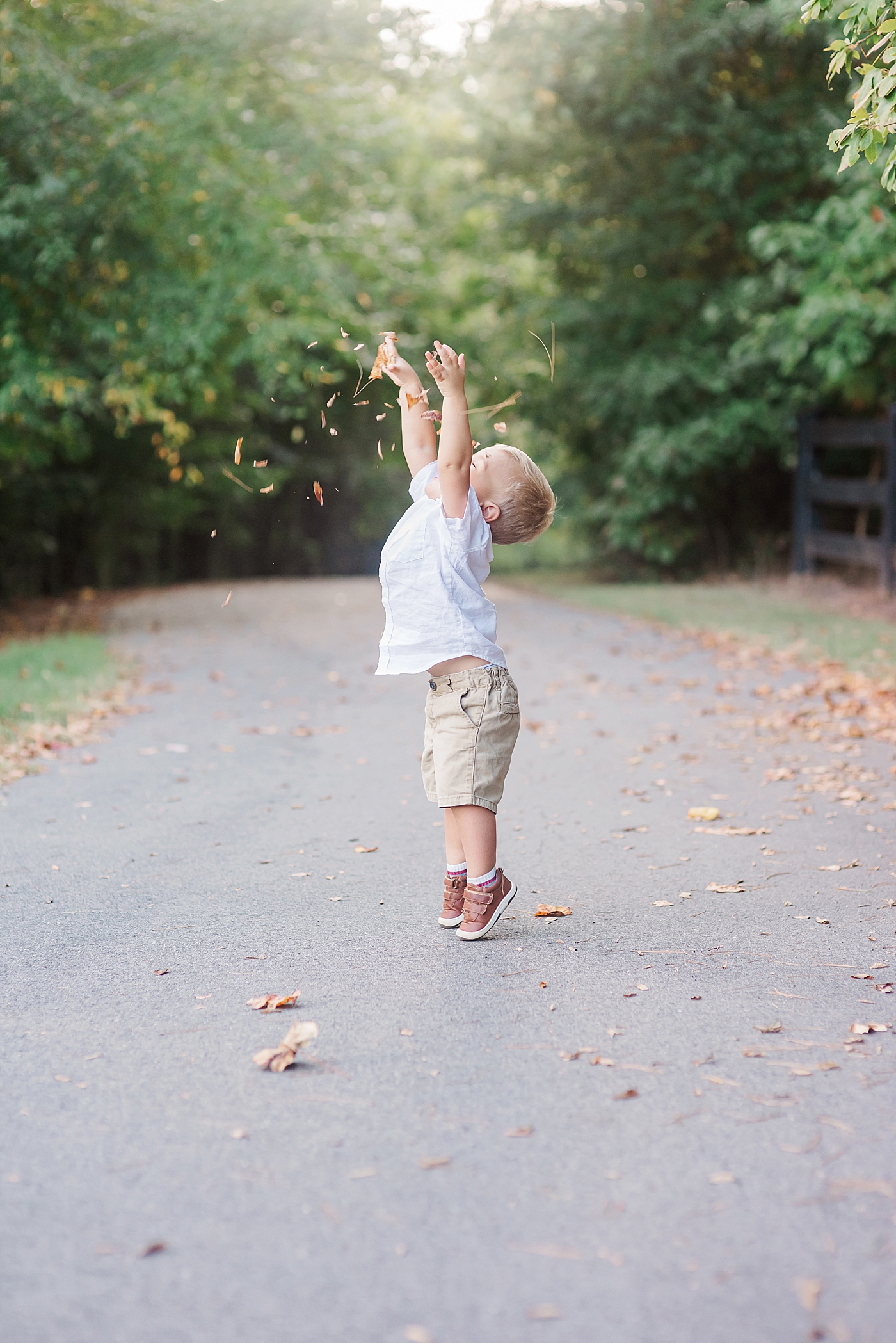 Little boy throwing leaves on a path | Photo by Anna Wisjo