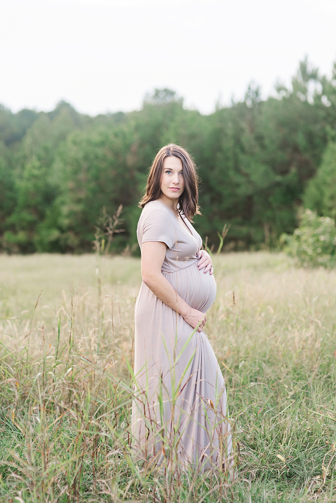 Beautiful mom to be standing in a field | Photo by Anna Wisjo