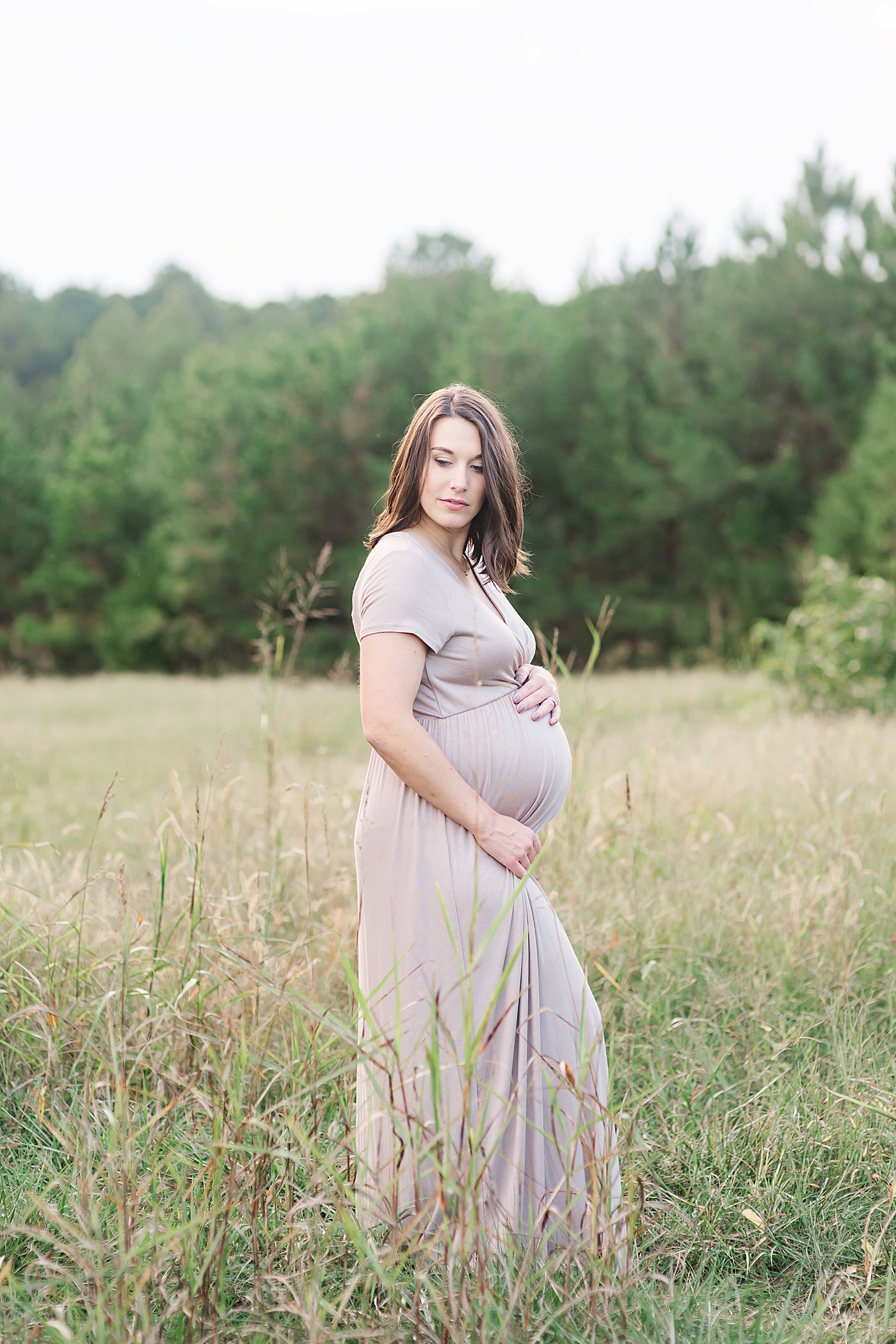 Mom to be in mauve dress standing in a field | Photo by Anna Wisjo