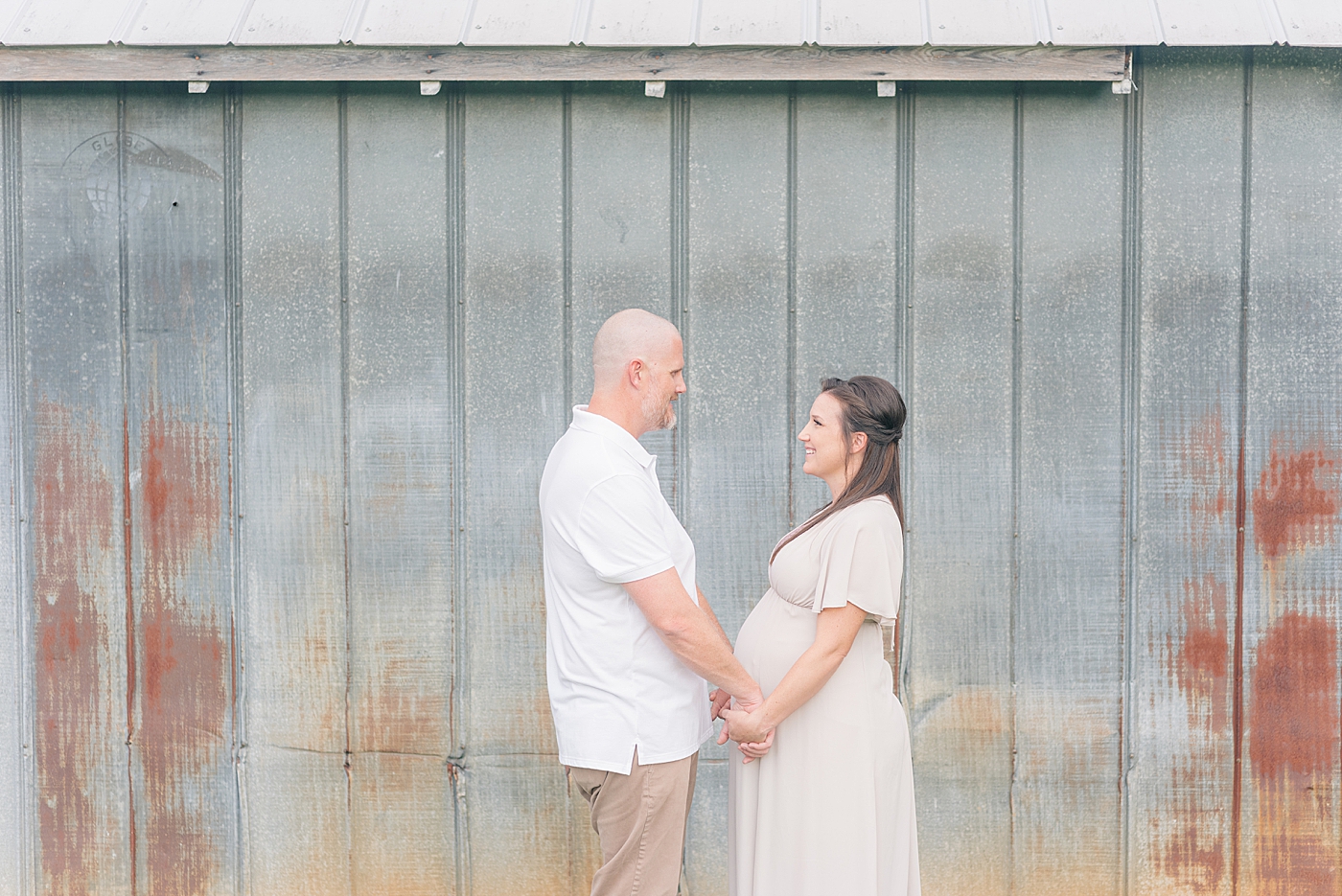 Mom and dad to be holding hands in front of a barn | Photo by Anna Wisjo Photography
