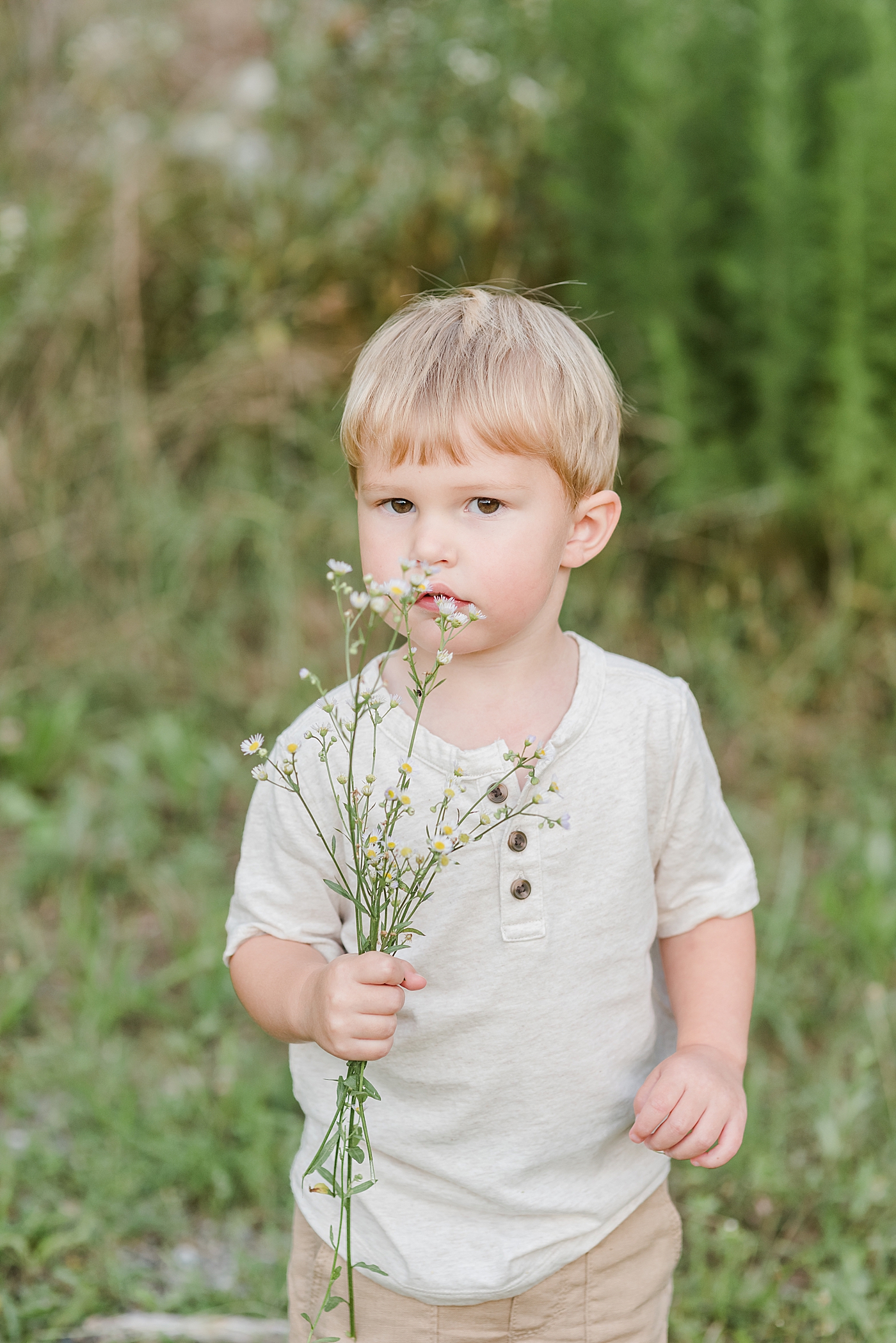 Little boy in cream shirt smelling flowers | Photo by Denver NC Maternity Photographer Anna Wisjo