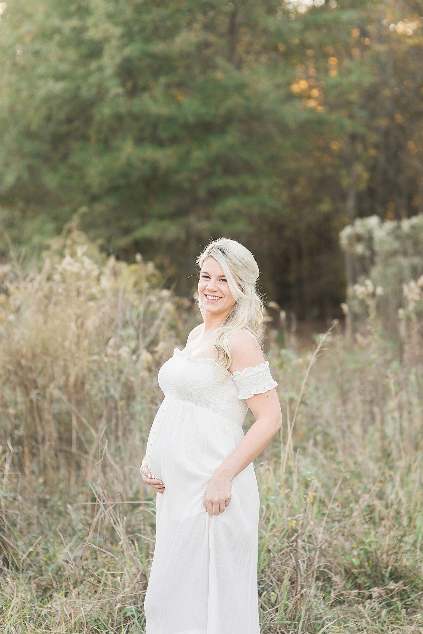 Expecting mother in long white dress in a field | Photo by Charlotte Maternity Photographer Anna Wisjo 