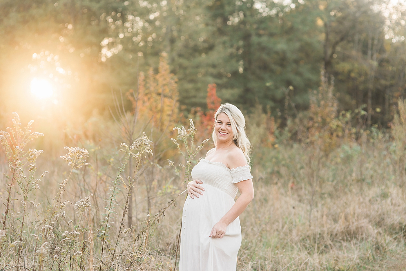 Mom to be in long white dress in a field at sunset | Photo by Anna Wisjo 