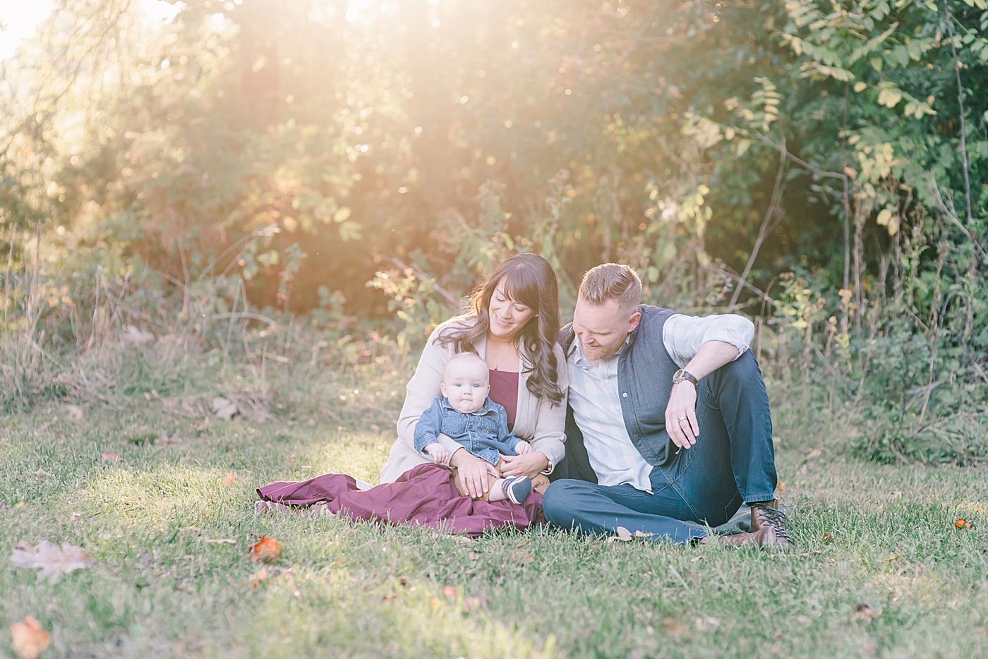 Mom and dad sitting with baby in the grass | Photo by Anna Wisjo Photography