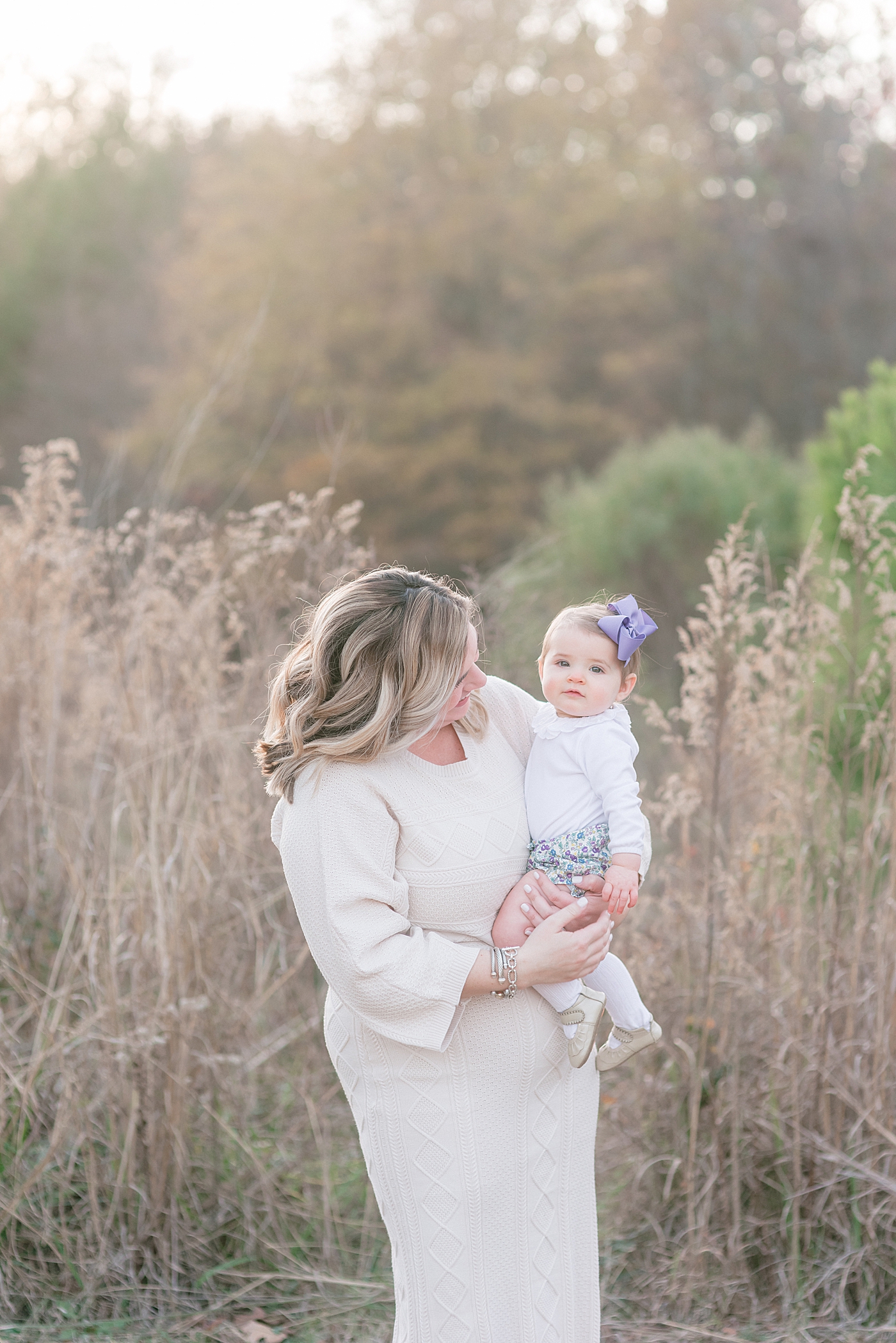 Mom and baby girl in white in a field at Milestone Session at Marvin Efird Park | Photo by Anna Wisjo Photography 