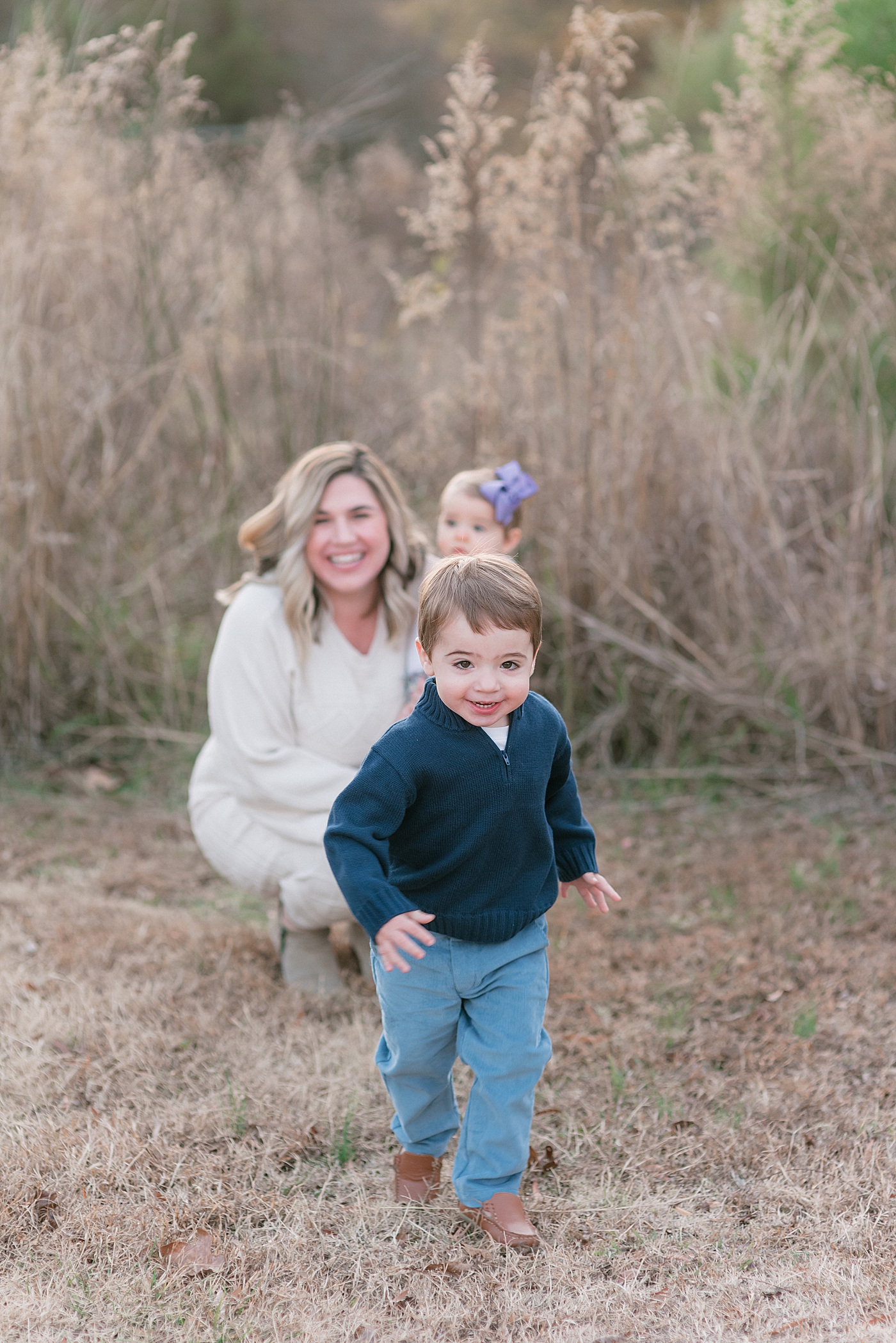 Little boy in navy running with family in the background | Photo by Anna Wisjo Photography 