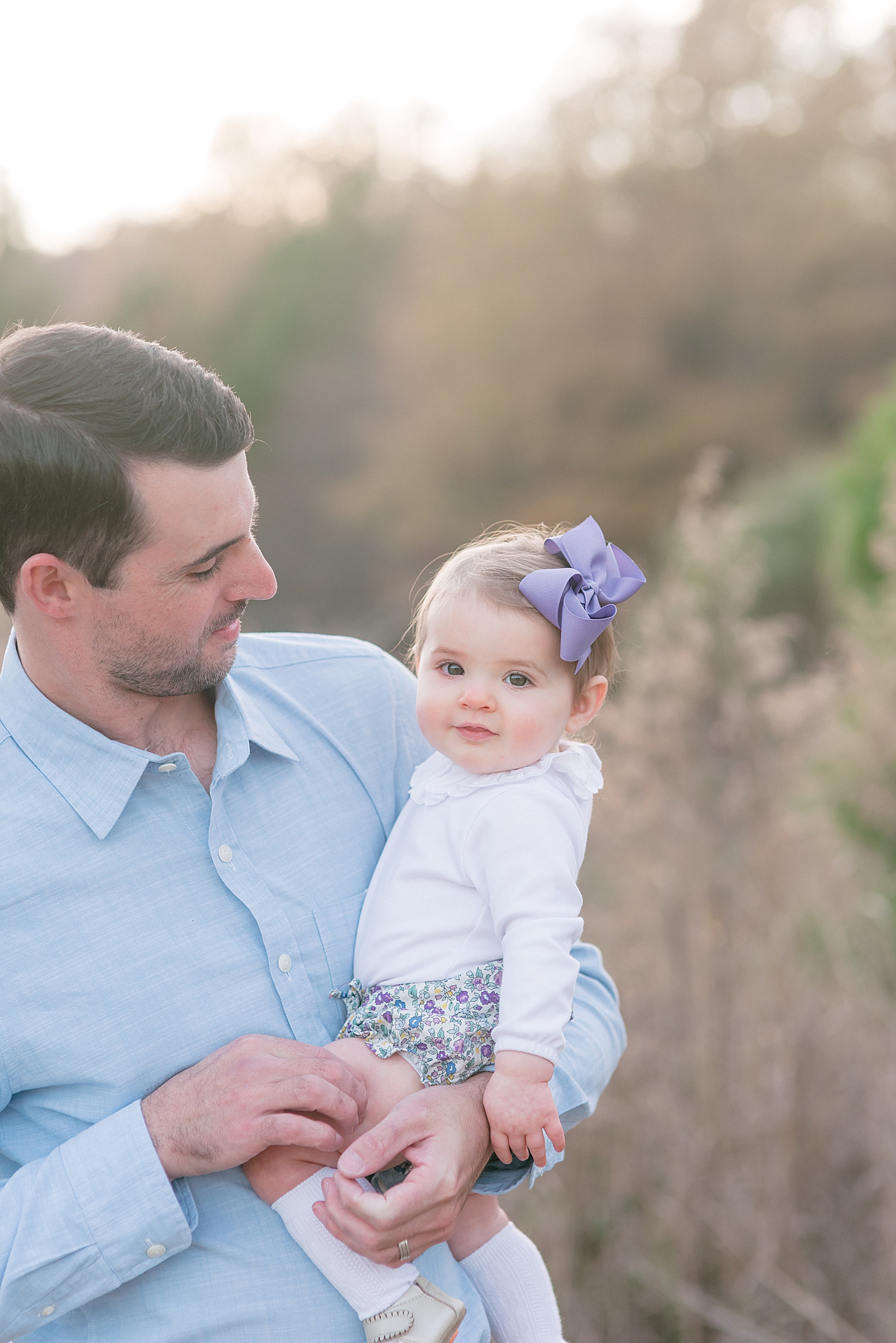 Daddy smiling at baby girl with purple bow during her Milestone Session in Charlotte | Photo by Anna Wisjo Photography 