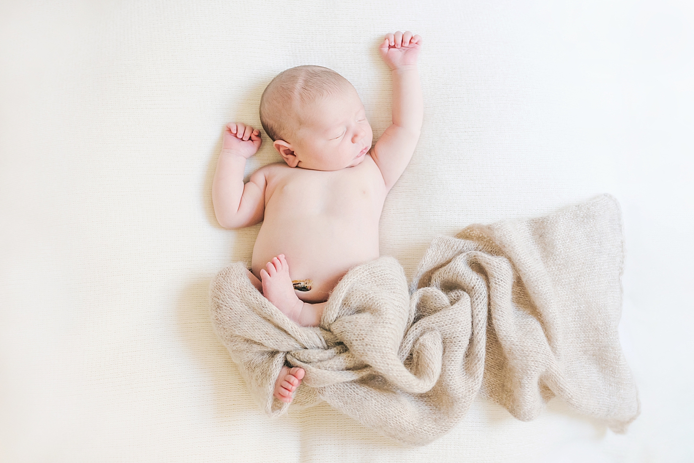 Newborn baby boy stretching in a tan swaddle | Photo by Anna Wisjo Photography