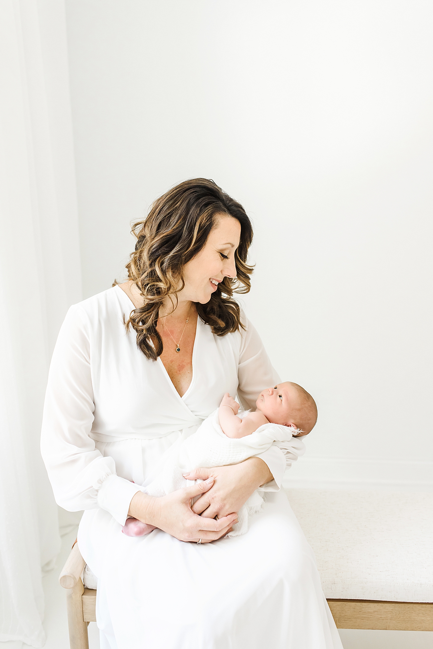 Mom in a white dress smiling at her new baby | Photo by Anna Wisjo Photography
