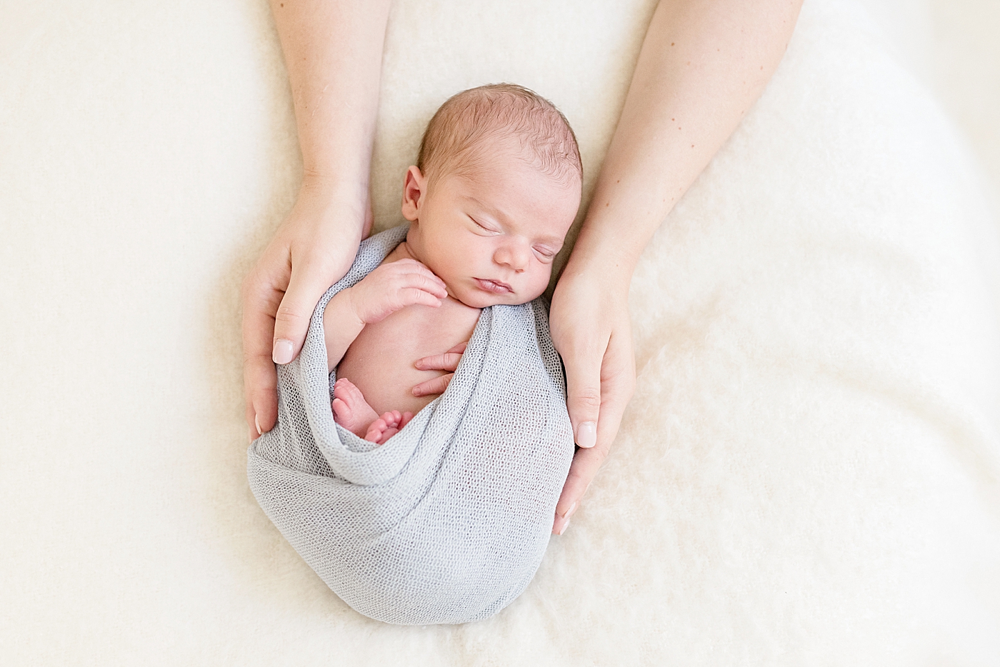 Baby in gray swaddle with mom's hands | Photo by Anna Wisjo Photography