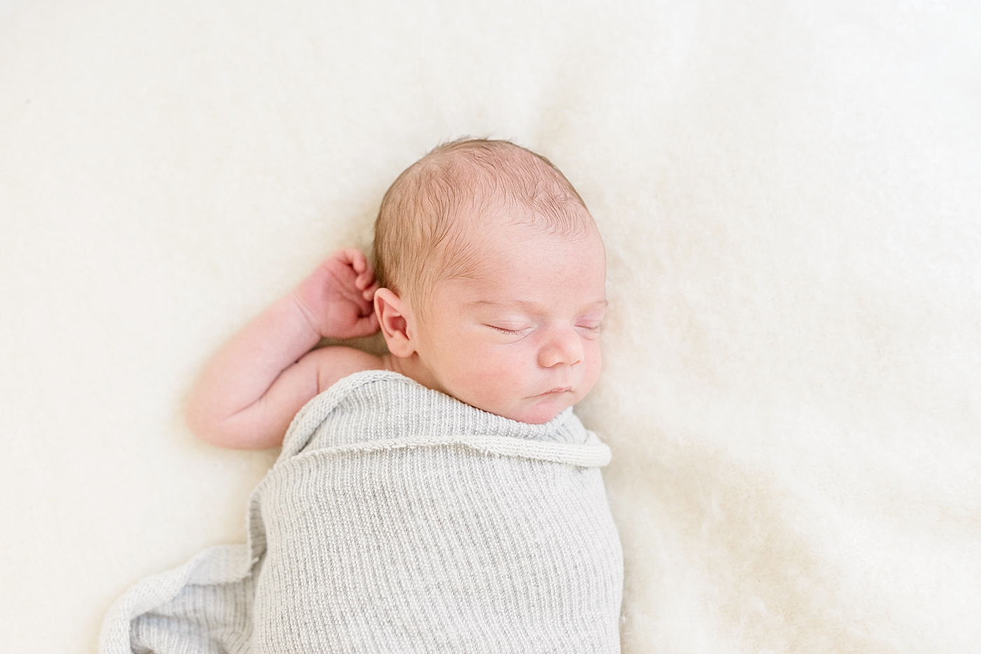 Newborn baby boy wrapped in a gray swaddle | Photo by Anna Wisjo Photography