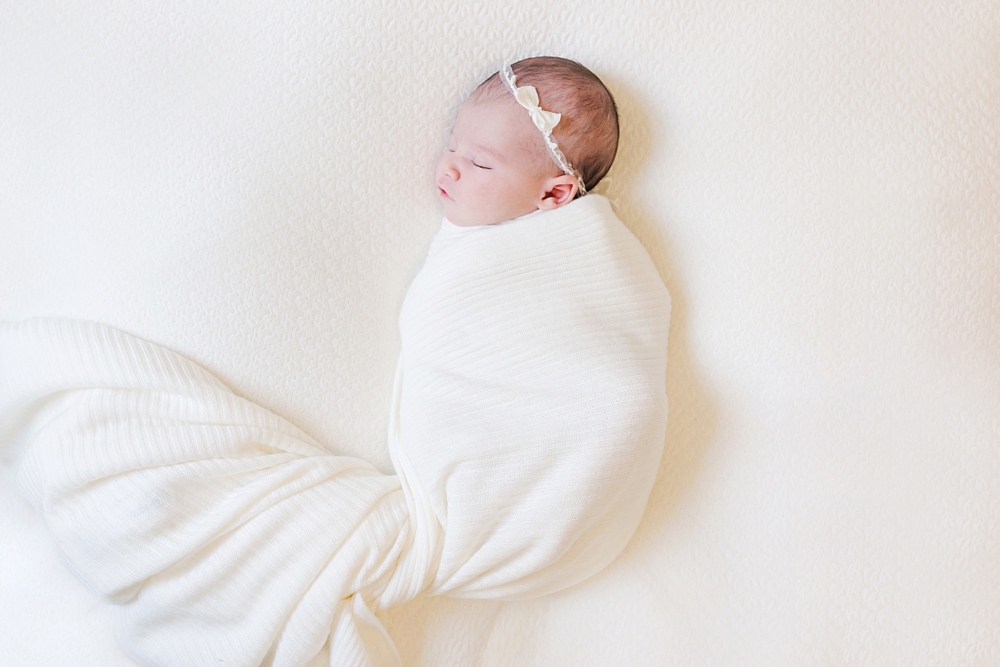 Newborn baby girl wrapped in a white swaddle | Photo by Anna Wisjo Photography
