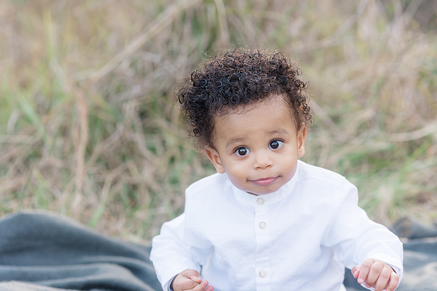 Baby boy in a white shirt sitting on a blanket | Photo by Anna Wisjo Photography