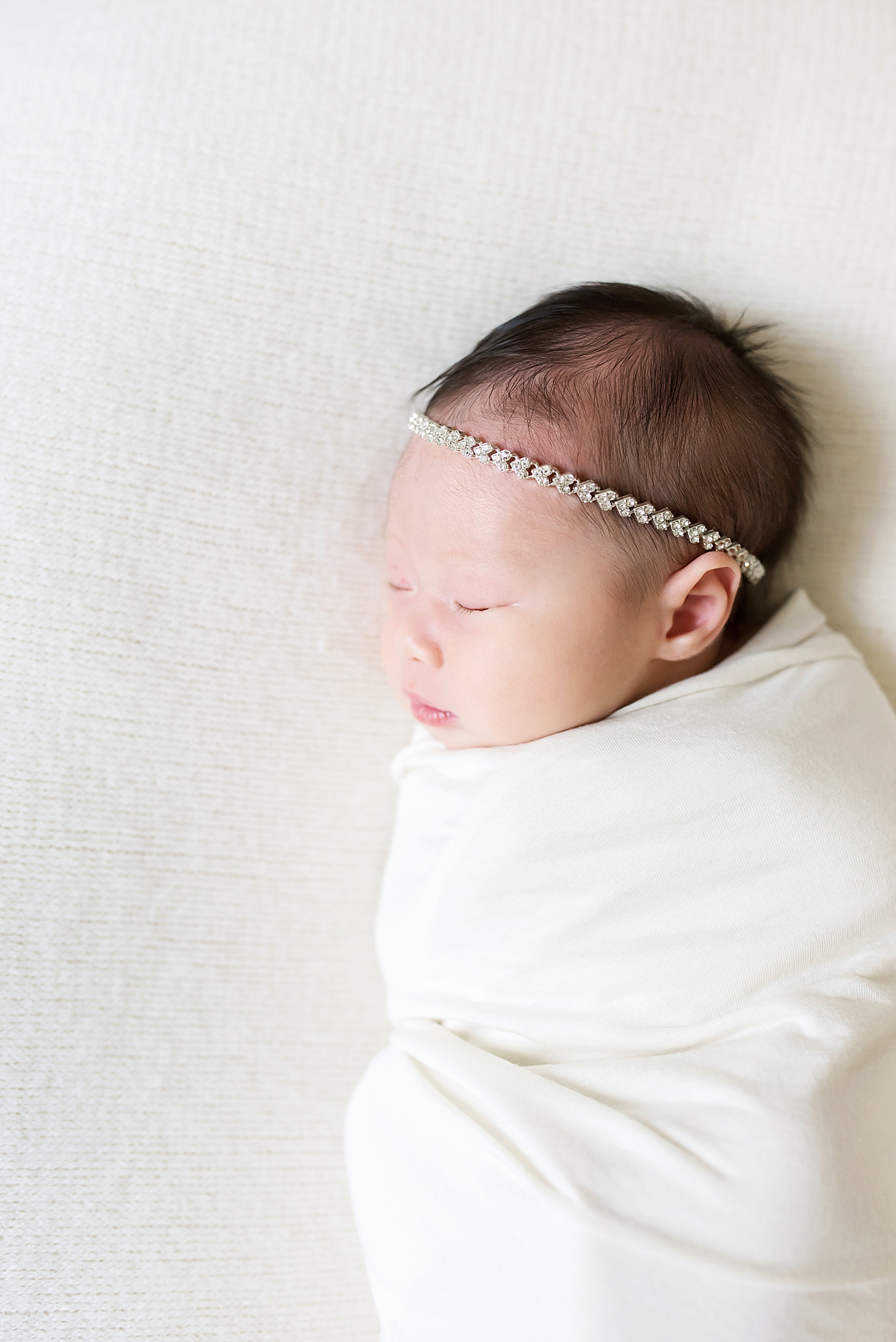 Baby girl with headband asleep in a white swaddle | Photo by Anna Wisjo Photography
