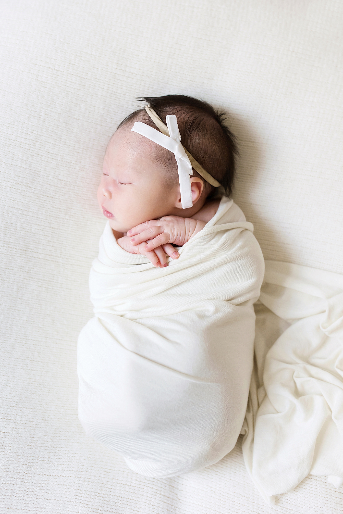 Baby girl wrapped in a white swaddle with a bow headband | Photo by Anna Wisjo Photography