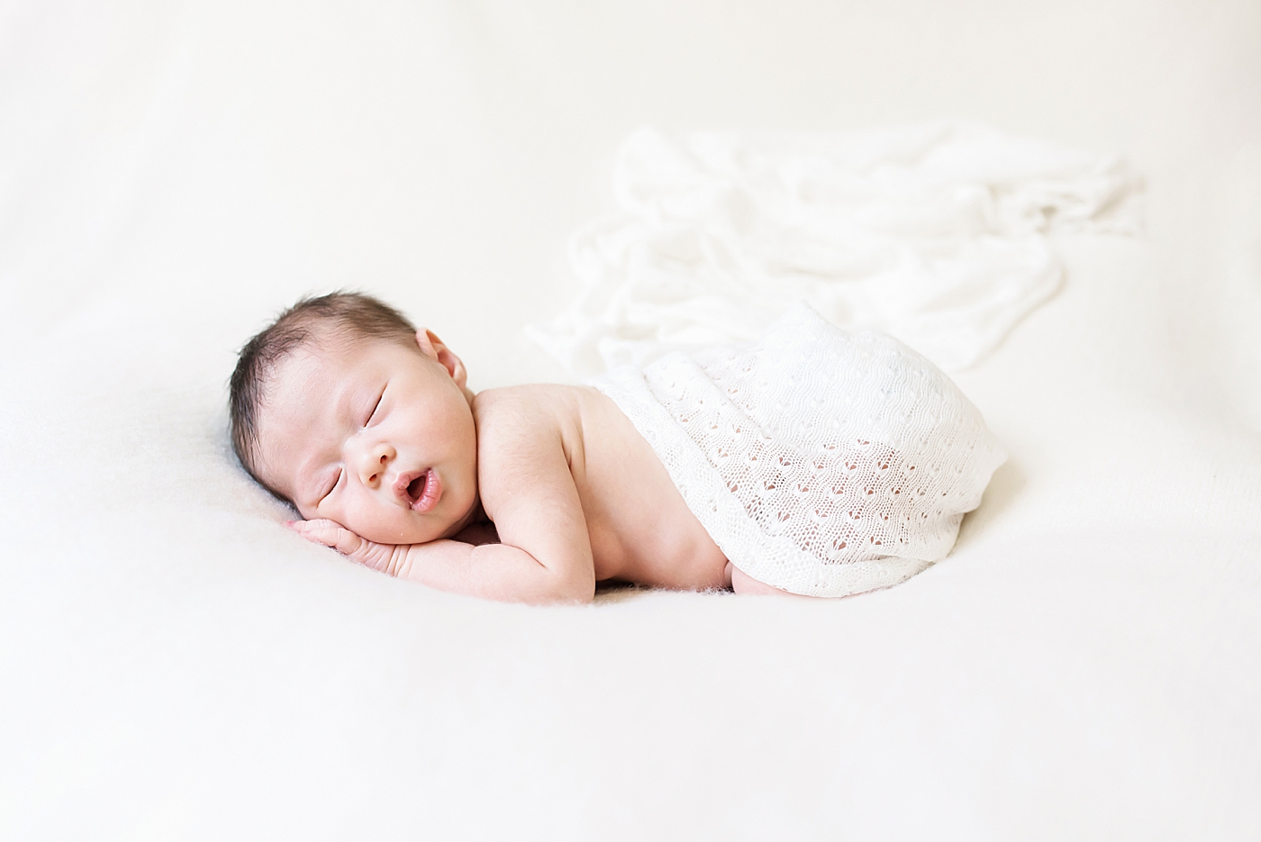 Sleeping newborn baby girl wrapped in a white blanket | Photo by Anna Wisjo Photography