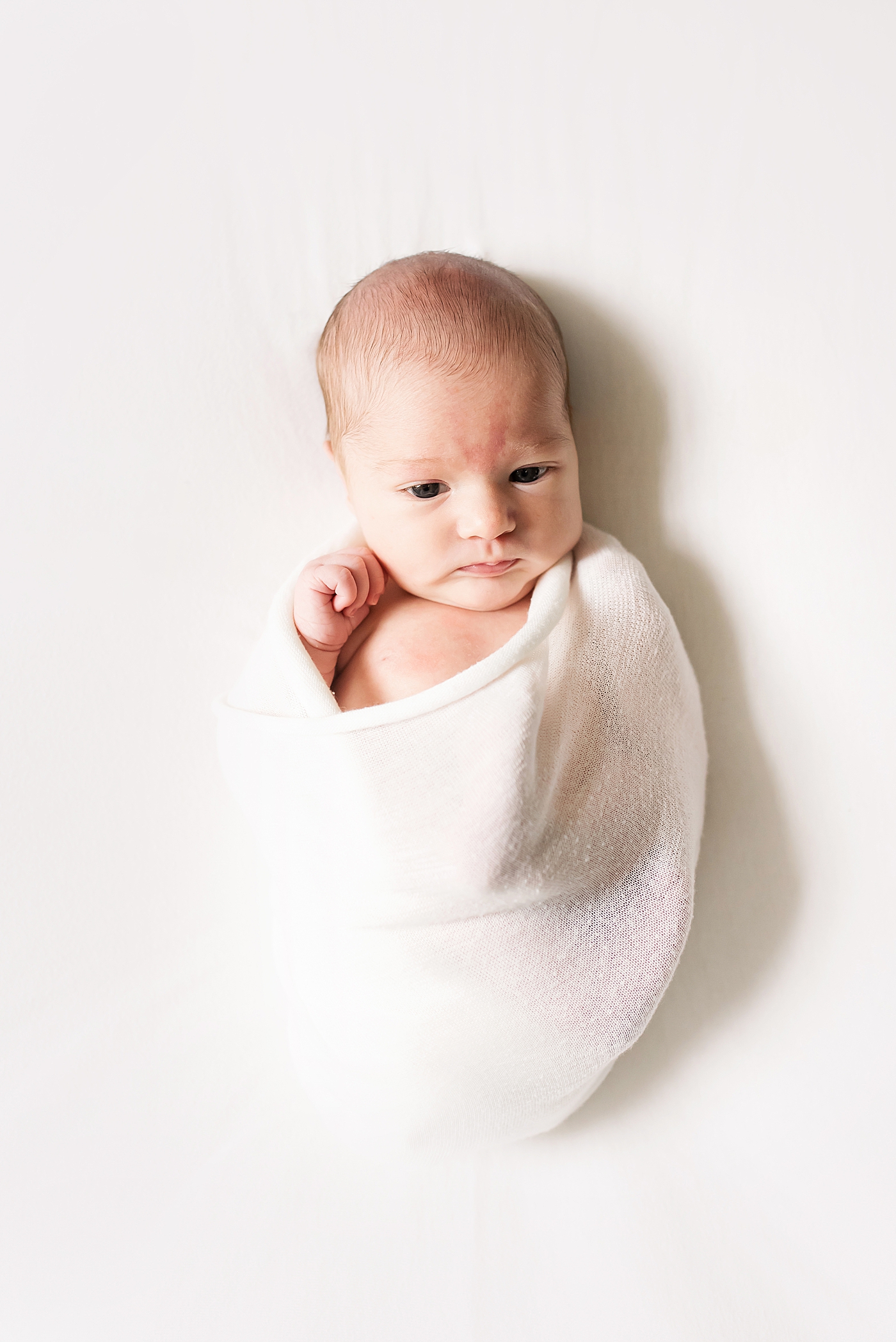 Baby girl awake wrapped in a white swaddle | Photo by Anna Wisjo Photography 