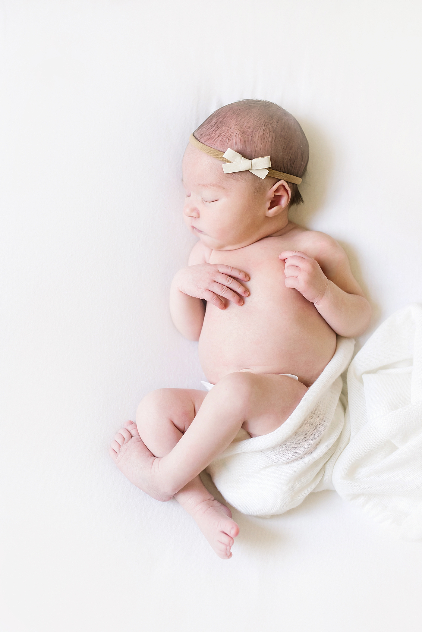 Sleeping newborn baby girl with a bow in a white swaddle | Photo by Anna Wisjo Photography 