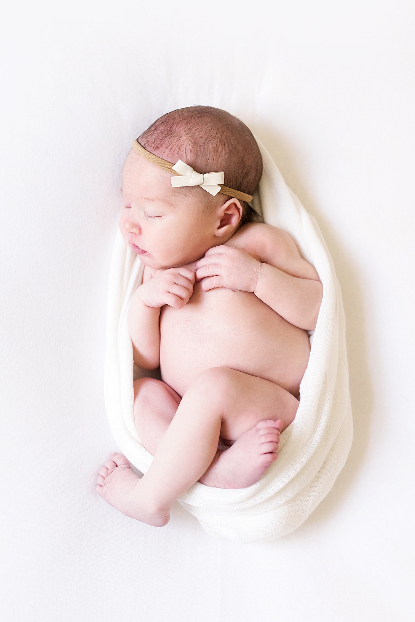 Baby girl wrapped in a white swaddle with a bow headband | Photo by Anna Wisjo Photography 