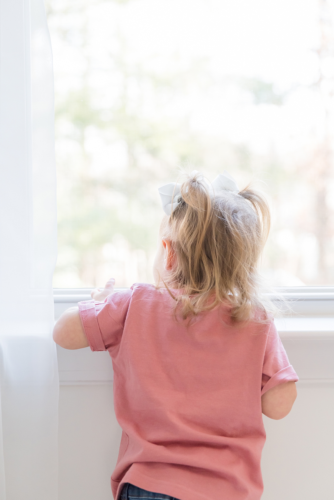 Little girl in a pink shirt looking out the window | Photo by Charlotte Milestone Photographer Anna Wisjo Photography