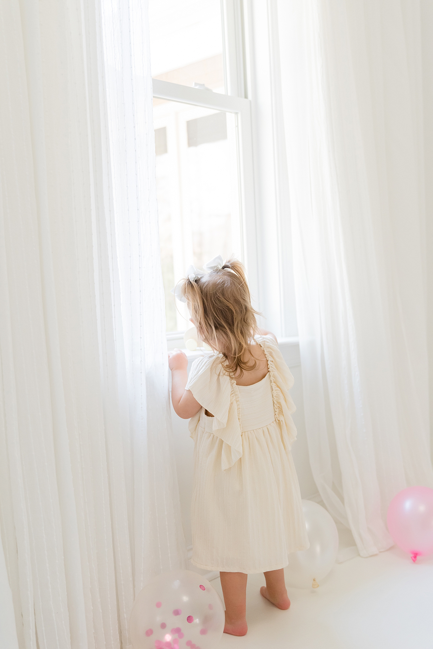 Little girl in a white dress looking out a window | Photo by Anna Wisjo Photography