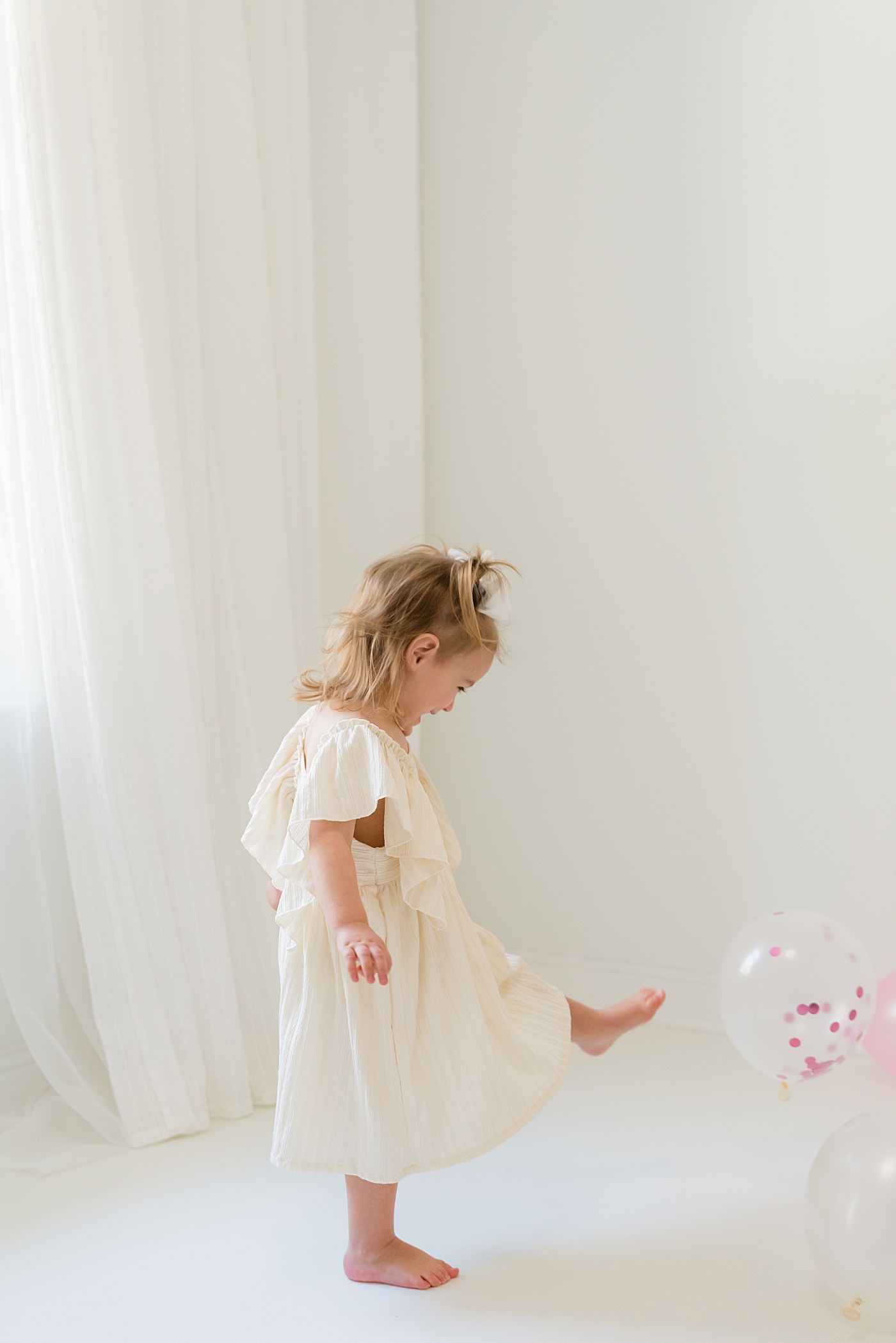 Little girl in white dress kicking balloons in the studio | Photo by Anna Wisjo Photography